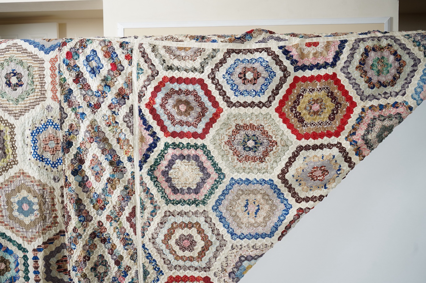 A large 19th century ‘Grandmother’s Flower Garden’ cotton patchwork bedspread, using dress fabric scraps from the day to create hexagonal concentric patterns which form a flower like shape/pattern, 282 x 254cm. Condition